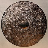 An ornate disc made out of silver, covered with an intricate pattern.