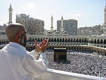 A man raising his hands in prayer in front of the Kaaba