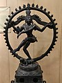 Pictures clicked in Telangana State Archaeology Museum, Hyderabad, India.Title: NatarajaProvenance: Motupalli, Prakasam district.Acc. no. 78-35In this fine bronze of the Chola period, Shiva is seen as supreme god and lord of dance, Nataraja. The god is shown in the nandatandava. In this upper right hand he holds a drum, representing primordial sound of creation. The upper left hand holds a flame of destruction, that both destroys and cleanses the impurity of the soul, indicating the opposite in his nature that are symbolized by both female and male earrings.He makes the gesture 'Have to fear' and points to his raised left foot, symbolizing release or place of refuge and salvation for the worshipper. He treads upon the prostrate dwarf of ignorance, and illusion. Apasmara and the sense of ego which a devotee must overcome. The diminutive figure and goddess Ganga appears in his flowing hair. The god maintains an exquisite poise and equanimity at the centre of the whirling cycle of cosmic activity, symbolized by the flaming circle.