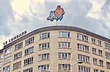 Photographie montrant le haut d'un immeuble, surmontée d'une enseigne à l'effigie de Tintin et Milou.