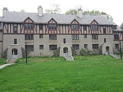 Ein dreistöckiges graues Tudor Revival-Gebäude mit rötlichen Balken steht an einem bewölkten Tag vor dem grünen Rasen.