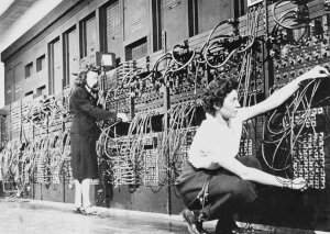 Two women plugging cables on the wall-sized computer