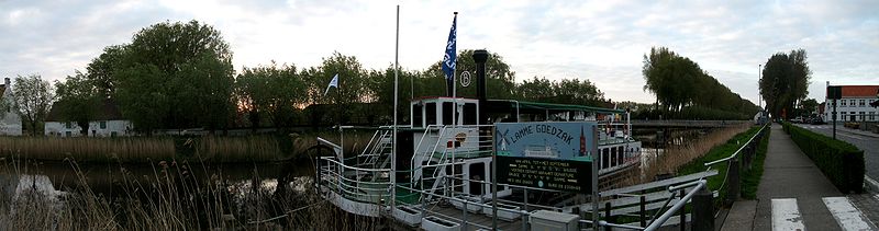 Een panoramafoto van de Damse Vaart met de toeristische boot 'Lamme Goedzak' op de voorgrond.