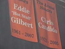 To oransje bannere som henger fra taket i en hall.  Til venstre står Eddie Gilbert og på den andre Chris Candido.