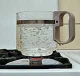 Bubbles form and rise from the bottom of a glass container on a gas ring, to break at the surface of a pot