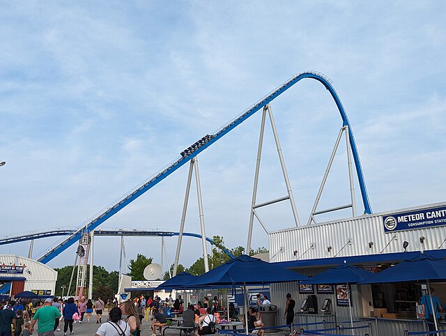 A blue roller coaster's first drop, with a 8 car train about to go down it.