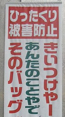 A caution written in Kansai dialect. The warning, Kii tsuke yā, Anta no koto ya de, Sono baggu, translates as Take care! Do not let your bag get snatched!