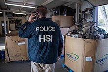 Photo of a member of Homeland Security Investigations standing nearby pallets of catalytic converters seized during Operation Heavy Metal