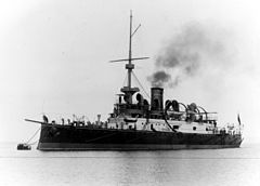 Czarno-biała fotografia przedstawiająca SMS „Wien” na morzu. Widok sprzed lewej burty. Na dziobie jednostki trzech marynarzy, na pokładzie rufowym widocznych jest kolejnych kilka sylwetek marynarzy