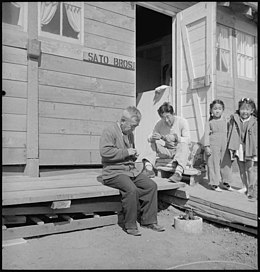 Father and son while away the hours carving small wooden animals for the children in front of their home in the barracks. Lange, 1942. San Bruno, California. Father and son while away the hours carving small wooden animals for the chi . . . - NARA - 537905.jpg