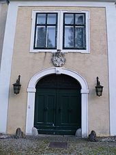 Frontalansicht des Torbaus mit einem korbbogigen Tor, darüber ein steinernes Wappenrelief und ein gekuppeltes Fenster