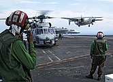 US Navy 050104-N-1229B-019 An SH-60B Seahawk helicopter waits to take-off as a C-2A Greyhound lands carrying mail and military personnel aboard USS Abraham Lincoln (CVN 72).jpg
