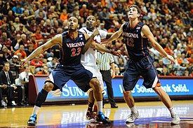 Un jugador de baloncesto universitario vestido de blanco con un borde naranja y azul se prepara para lanzar un tiro libre.