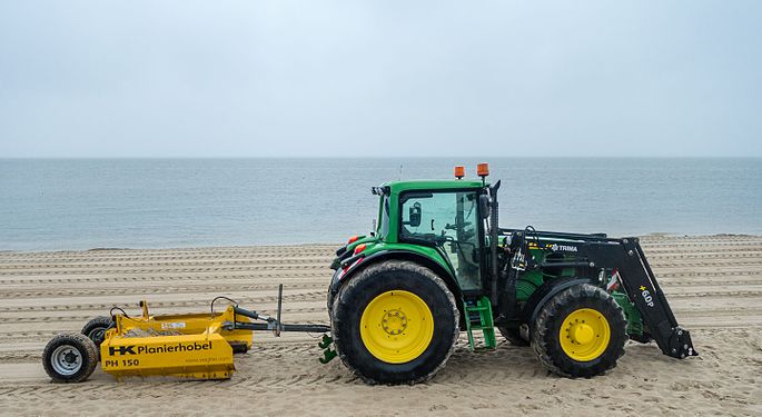 Traktor mit Planierhobel zum ebnen des Strandes. Tractor with planer for paving the beach.