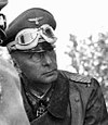 The head and torso of a man wearing a military uniform and overcoat; an Iron Cross is displayed at the front of his uniform collar.