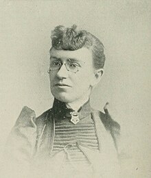B&W portrait photo of a woman with her hair in an up-do, wearing glasses and a dark blouse.