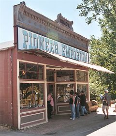 Photograph of a historic store, the Pioneer Emporium, in the Columbia Historic District. The building sports a tall false front, and several visitors stand in the shade of an awning.