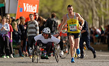 A runner gives a friendly tap on the shoulder to a wheelchair racer during the Marathon International de Paris (Paris Marathon) in 2014. David Bizet - Marathon de Paris 2014.jpg