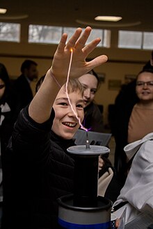 Boy allowing arc from Tesla coil to strike hand. He feels no pain Energy is among us.jpg