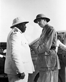 Éboué, en kraftig sort mand iført hvid uniform og hjelmhjelm, vender ud mod Charles de Gaulle, en hvid mand i lignende, men mørkere farve.