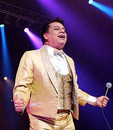 Juan Gabriel, singing in a light-colored suit