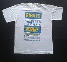 This is a white t-shirt on a black background. The lettering is blue on white and yellow on blue. It says, "Rights for Disabled People Now!" and "Disabled People & Manchester Making It Happen".