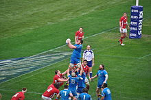 Photographie d'une touche lors d'un match de rugby entre les Italiens en maillots bleus et les Gallois en maillots rouges.