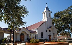 Medium sized white church with small steeple and red roof surrounded by some plant beds with brick borders.