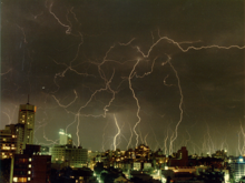 Ciel nuageux dans lequel se trouvent des dizaines d'éclairs, au-dessus d'une ville.