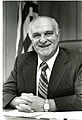 Portrait of a smiling Dr. Ernest Ambler in dark suit and striped tie