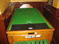 A bar billiards table, showing the holes but not the mushrooms that are placed in front of the holes. All players stand in front of the table (no side access is permitted).