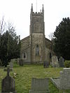 Stone building with prominent square tower at near end. In the foreground are gravestones and trees to the left and right.