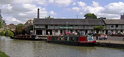 Water with two narrow boats. And bridge. On the: far side is: a white coloured building displaying banner which says Canal Museum and 