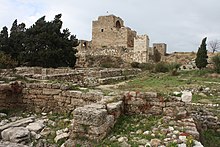Billede af gamle ruiner med cypresser og et befæstet slot i baggrunden