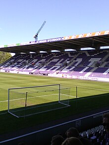 Zdjęcie przedstawiające bramkę, boisko oraz trybunę stadionu z napisem „BEERSCHOT” na siedzeniach.