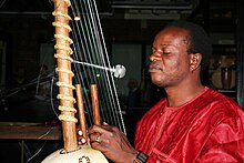 Jali Fily Sissokho playing a kora tuned with konso (braided leather ring) string terminations. Kora-Player2.jpg