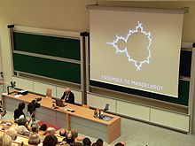 Benoit Mandelbrot during his speech at the ceremony when he was made an officer of the Legion of Honour on September 11, 2006, at the Ecole Polytechnique
; here, with a display of the Mandelbrot set. Mandelbrot p1130876.jpg