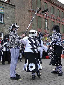 Pig Dyke Molly, in their distinctive black-and-white costumes, performing a broom dance at Whittlesea Straw Bear PigDykeMollyBroomDance.jpg