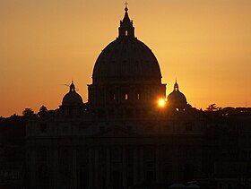 La malhela silueto de la kupolo de St. Peter metita kontraŭ la oranĝo, vesperĉielo kaj malsupreniranta suno.