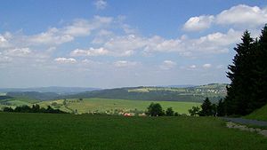 Blick vom Eckartsberg auf Schnett und den Simmersberg (780,8 m, rechts) mit seinem Nebengipfel Kohlberg (730,3 m, Mitte). Dazwischen ist im Hintergrund der Adlersberg (849,9 m) mit dem Neuhäuser Hügel (890,6 m) erkennbar. Links des Kohlberges folgen im Hintergrund das Gewerbegebiet Suhl-Friedberg und der Kleine Thüringer Wald mit Schleusinger Berg (663,2 m)  und Schneeberg (692,4 m). Mittig im Vordergrund der Ort Waffenrod/Hinterrod.