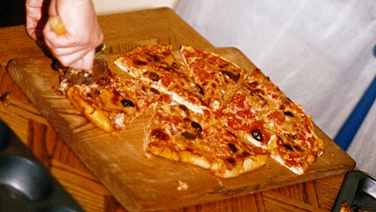 A baked pizza being sliced into sectors with a pizza cutter, to be served as finger food
