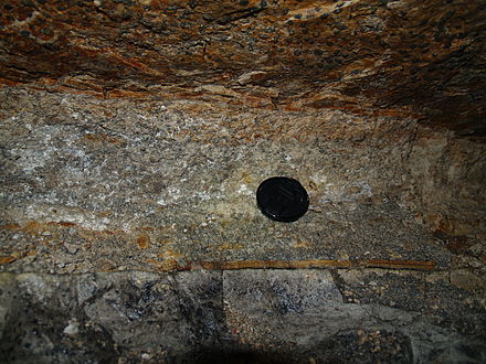 454 million-year-old volcanic ash between layers of limestone in the catacombs of Peter the Great's Naval Fortress in Estonia near Laagri. This is a remnant of one of the oldest large eruptions preserved. The diameter of the black camera lens cover is 58 mm (2.3 in).