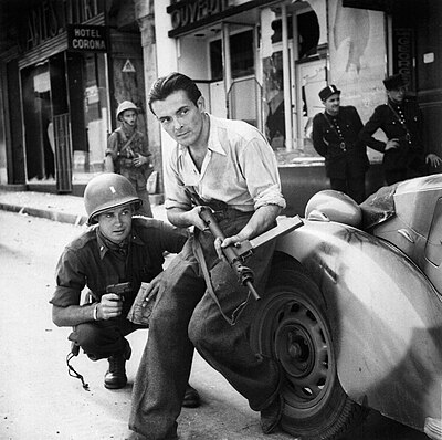 NARA caption: "American officer and French partisan crouch behind an auto during a street fight in a French city."