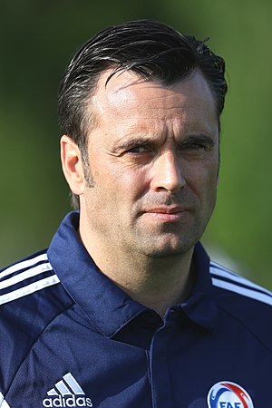 A man with dark hair wearing a dark tracksuit jacket.