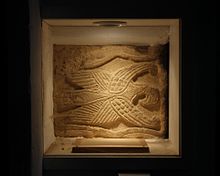 Anglo-Saxon relief just inside the Norman south door, representing the eagle of St John the Evangelist. It was an arm of a cross and may be 9th-century. Brixworth AllSaints Eagle.jpg