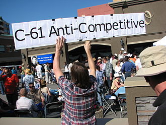 An opponent of the proposed Bill C-61 holds up a protest sign at a public breakfast event held during the Calgary Stampede by Canadian Industry Minister Jim Prentice. Canada Bill C-61 Opposition.jpg