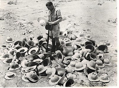 Original caption: “AFRICA – A BRITISH SOLDIER PICKS HIMSELF OUT A SUN HELMET FROM A PILE OF THEM WHICH WERE LEFT BEHIND WHEN ITALIAN TROOPS LEFT THE SCENE HURRIEDLY SOMEWHERE ON THE WESTERN DESERT.”, Commonwealth forces despatch, June 1941