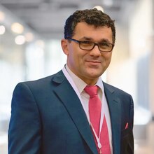 Josef Hammer, author and social justice advocate, wearing a dark blue suit with a white shirt and pink tie, in a professional setting.