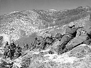 A line of soldiers on a hill under a boulder engaged in a battle