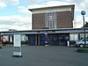 Een gebouw met rode bakstenen en een rechthoekig, donkerblauw bord met de tekst "NORTHFIELDS STATION" in witte letters, allemaal onder een lichtblauwe lucht